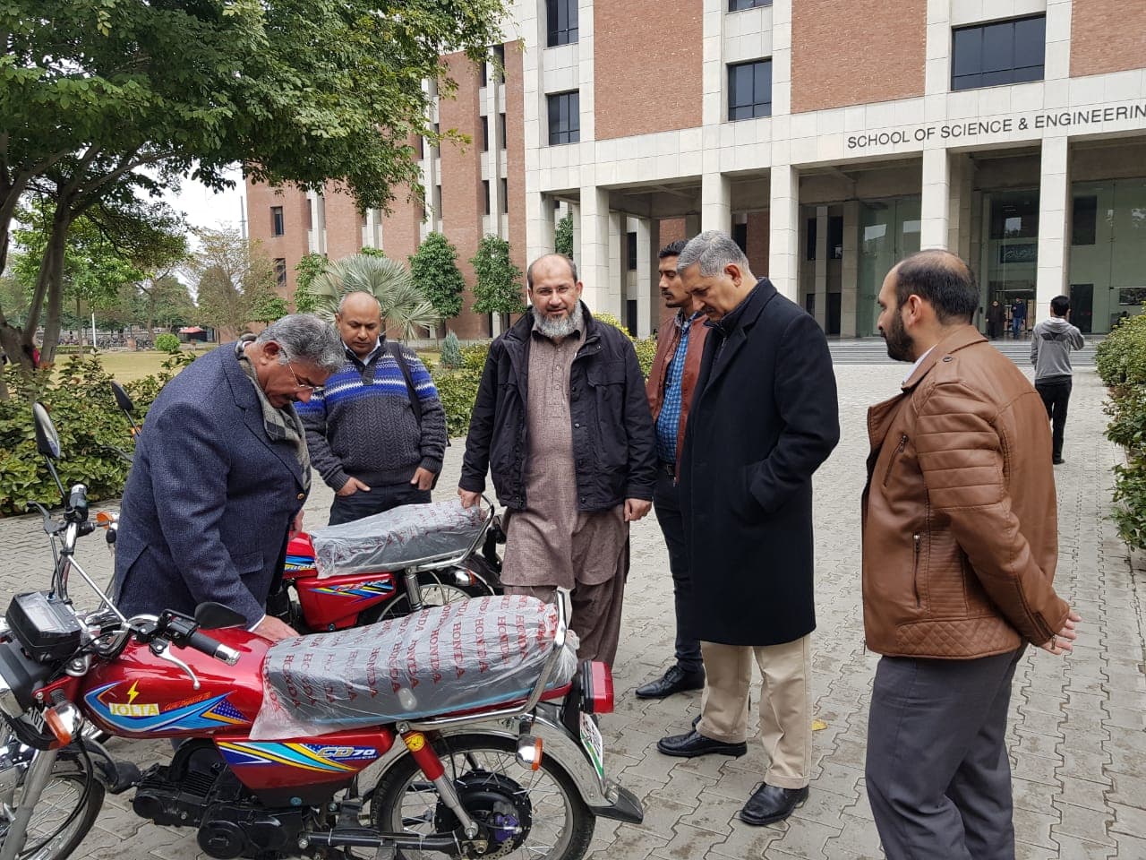 Irfan Ahmed and LUMS professors examining two Jolta electric motorcycles on campus